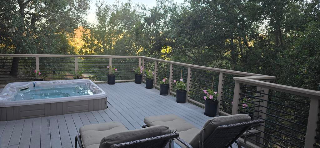 Outdoor hot tub on a deck with chairs and potted plants surrounded by trees