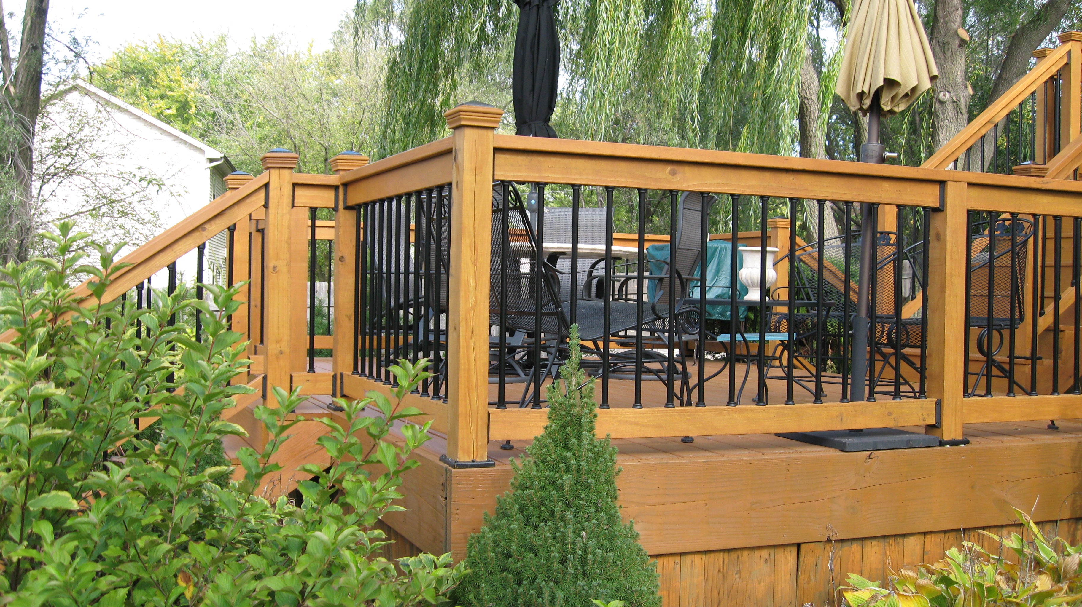 Wooden deck with railing and outdoor furniture, surrounded by greenery